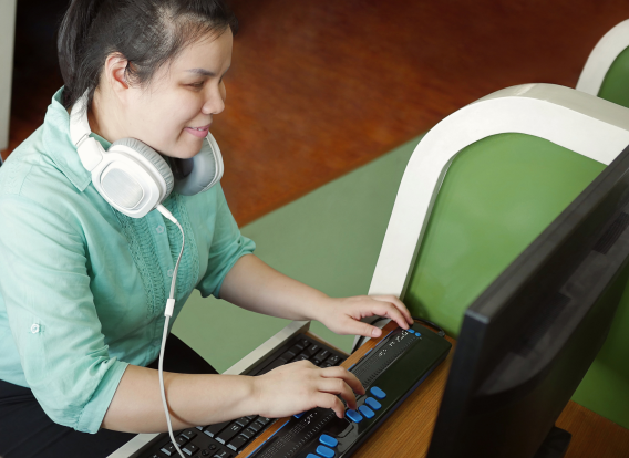 Blind girl using a computer with headphones and assistive technology.